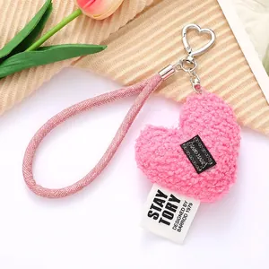 Pink plush heart keychain with woven lanyard and handmade label displayed on soft fabric
