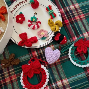 Close-up of handmade knitted Christmas charms featuring wreaths and bows on a checkered cloth