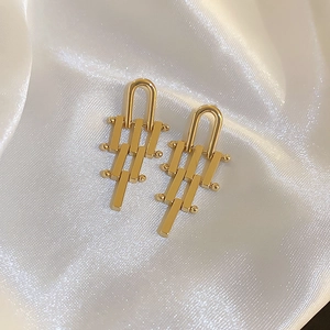 Minimalist gold geometric tiered earrings on white silk fabric background