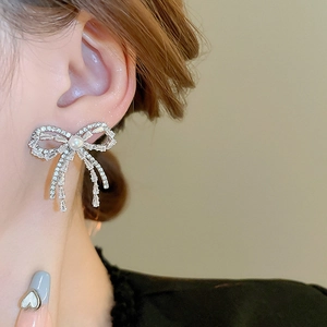 Close-up of sparkling bow earrings with rhinestones and pearl on model's ear