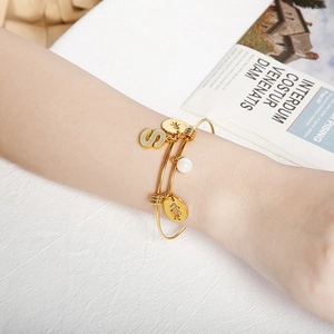 Detail of adjustable gold bangle with letter S charm and pearl on female wrist