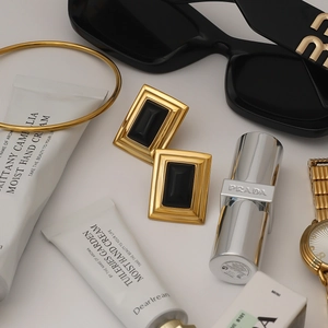 Flat lay showing gold geometric earrings with black rectangle stone and fashion items