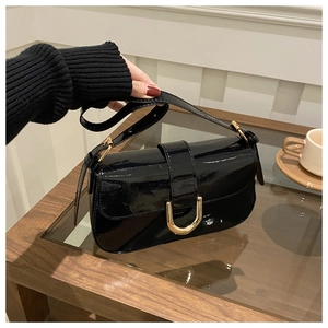 Close-up of black patent leather bag with gold horseshoe buckle and adjustable strap