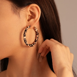Close-up of a large leopard print hoop earring worn by a model in a stylish studio setting