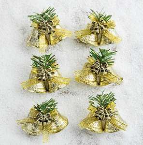 Detail of six gold Christmas bell ornaments with bows and pine needles on faux snow