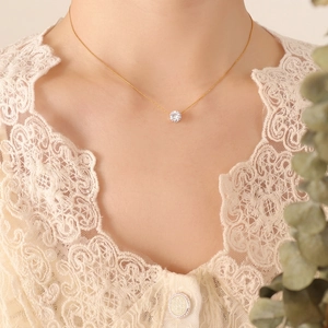 Minimalist gold necklace with a single round zircon pendant worn on a lace blouse