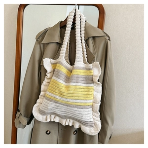 Detail of hand-knit striped tote bag with ruffles hanging against a beige trench coat