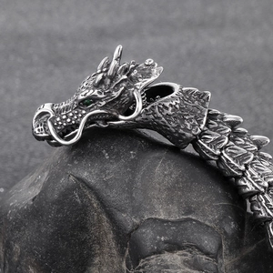 Close-up of vintage steel dragon head bracelet with green eyes on grey stone