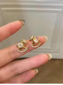 Detailed close-up of golden rocking horse stud earrings with sparkling white zircons