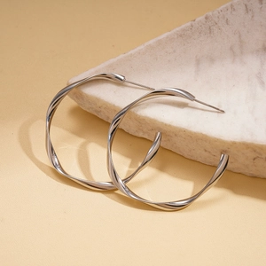 Close-up of geometric twisted silver stud earrings on a natural stone background
