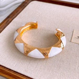 Detail of wide gold-finished cuff with white enamel inlay and textured radial metal patterns