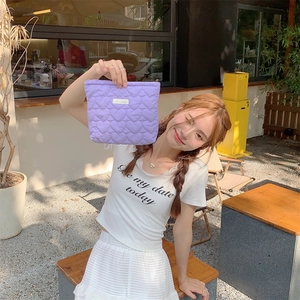 Detailed view of a purple quilted heart cosmetic bag held by a model in an outdoor setting