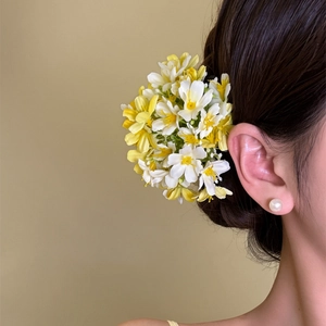 Detail view of yellow and white small floral hair clip on braided hair