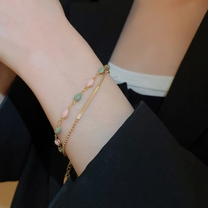 Detail of gold double-layer bracelet with pink and green enamel charms on a model wrist