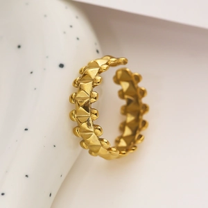 Macro detail of a golden ring with a geometric pyramid stud design on a white ceramic background