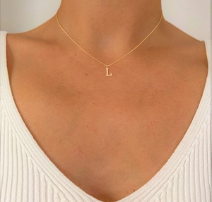 Detail of a minimalist gold stainless steel initial L pendant on a delicate chain