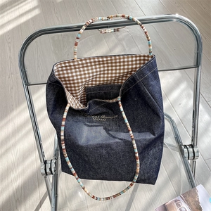 Detail of blue denim tote bag featuring plaid lining and colorful slim handles