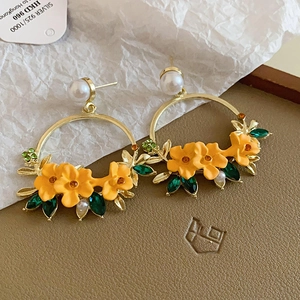 Detail of floral hoop earrings with yellow flowers, green crystals and pearl accents