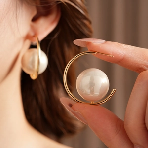 Close-up of elegant C-shaped gold hoop earrings with hanging pearl on model's ear