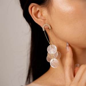 Close-up of safety pin gold earrings with sparkling crystals and white shell fringes