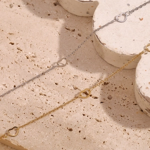 Detail view of gold and silver heart-shaped chain anklets on textured stone