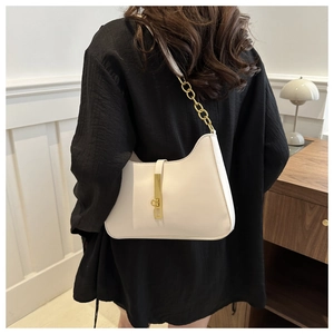 Detail view of white underarm bag with thick gold chain strap and metal lock closure
