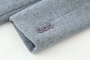 Close-up of grey wool blend coat sleeve featuring three tonal round buttons and fabric texture