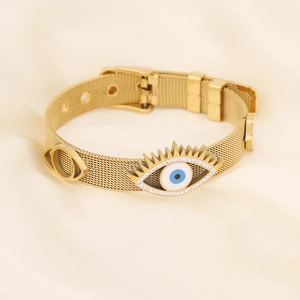 Gold evil eye mesh bracelet with crystal accents on a soft silk background