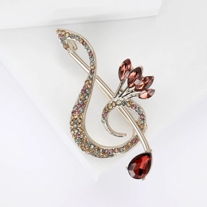 Detailed macro view of music note brooch with pink crystals and red teardrop pendant
