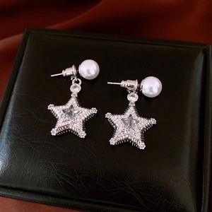 Macro shot of silver star earrings with inlaid zircon and round white pearls on black leather