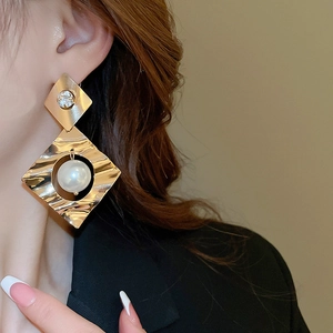 Detailed view of model wearing gold geometric diamond earrings with large pearls