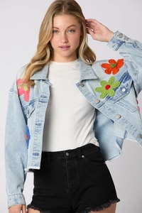 Detail of light blue denim jacket featuring colorful knit flower patches and fringe hem