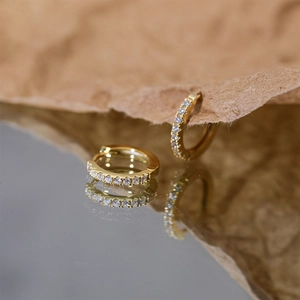 Close-up of golden S925 silver hoop earrings with clear square zircons on textured paper