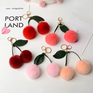 Cute cherry plush keychain with faux rabbit fur poms and green leather leaves on white background