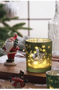 Close-up of frosted green glass Christmas candle holder with star patterns and warm LED lights