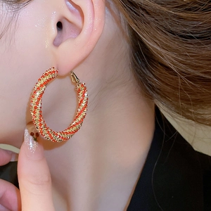 Macro shot of large red and gold woven bead hoop earring on a model ear