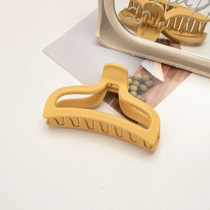Top view of a matte yellow claw clip on a minimalist white table with decor