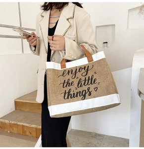 Dettaglio della borsa tote in lino con scritta enjoy the little things e manici marroni
