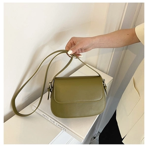 Detail view of a minimalist olive green leather crossbody bag held over a white book