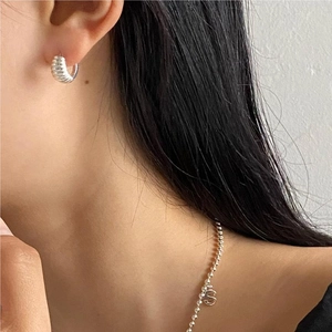 Detail of a woman wearing silver horn-shaped earrings and an S-letter pendant necklace