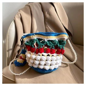 Detail of blue knit bucket bag with red cherry accents and elegant pearl bead strap
