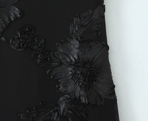 Detailed macro view of black 3D ribbon flower applique and textured knit fabric on dress