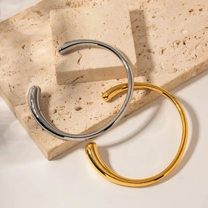Minimalist 18K gold and silver stainless steel open bangles on a beige travertine base