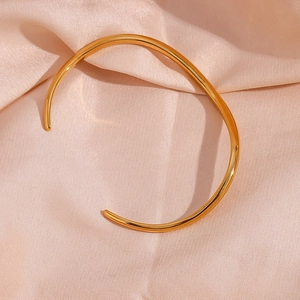 Detailed view of an irregular wave-shaped gold open bangle on soft pink silk fabric
