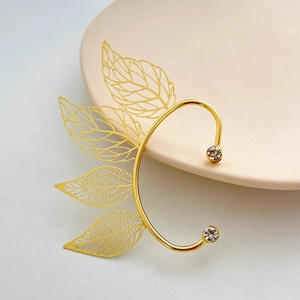 Elegant gold hollow leaf ear cuff with sparkling crystals on a minimalist ceramic tray
