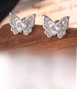 Detail of silver butterfly stud earring with heart zircon on a rustic wooden display