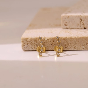 Elegant curved gold earrings with sparkling white cubic zirconia on a stone tray