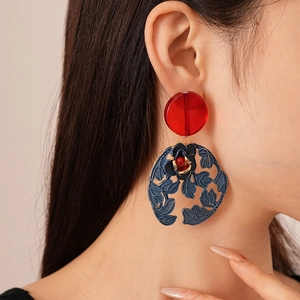 Detail of flower leaf earrings with red stud and dark blue floral circular pendant