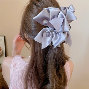 Detail of a large purple satin bow hair claw clip with gemstone center on model