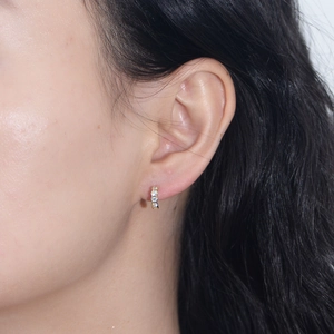 Close-up of a model wearing small gold geometric hexagon earrings with clear cubic zirconia